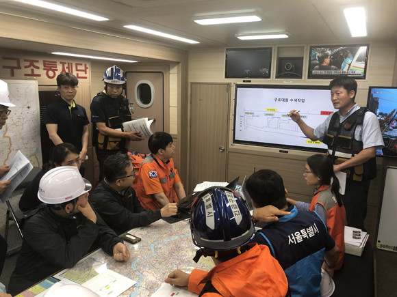 지난 7월31일 폭우로 서울 양천구 목동 저류배수시설에 투입된 작업자 2명과 이들을 대피시키기 위해 현장으로 들어갔던 안 모 현대건설 대리가 사망하는 사고가 발생했다. 작업자 투입 후 6분 뒤부터 비가 내리기 시작한 점을 감안하면, 안전불감증이 사고를 불러왔다는 비판을 피해가기 어려울 것으로 보인다. 사진은 박원순 시장과 소방대원 등이 구조통제단 본부에서 수색작업에 대한 설명을 듣는 모습. ⓒ 서울시