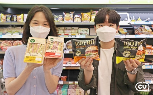 모델들이 CU의 새로운 햄버거 라인업 '100PRO 버거 시리즈' 제품을 들고 포즈를 취하고 있다.