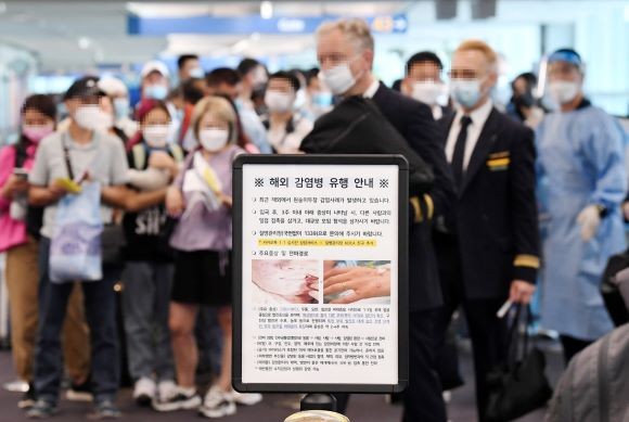 인천국제공항 제1터미널 입국장에 해외입국자들이 검역을 받기 위해 대기하고 있다. 승객들 앞에는 원숭이두창 관련 안내문이 세워져 있다. ⓒ 연합뉴스