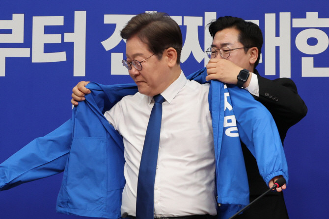 박찬대 더불어민주당 당대표 직무대행 겸 원내대표가 28일 서울 여의도 국회에서 열린 최고위원회의에서 이재명 대선 후보에게 선거운동용 파란색 점퍼를 입혀주고 있다. ⓒ 연합뉴스
