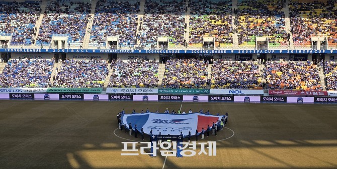 지난 2월 수원월드컵경기장에서 열린 K League 개막식에서 참가자들이 경기장 중앙에 모여 대형 깃발 퍼포먼스를 선보이며 시즌 개막을 알리고 있다. ⓒ 프라임경제