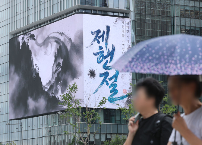 제78주년 제헌절인 17일, 도심의 한 건물 외벽 대형 전광판에 제헌절 기념 영상이 송출되는 가운데 시민들이 우산을 쓴 채 거리를 지나고 있다. ⓒ 연합뉴스